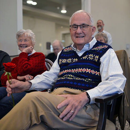 A man holds a rose and smiles, surrounded by fellow residents, during a community gathering.