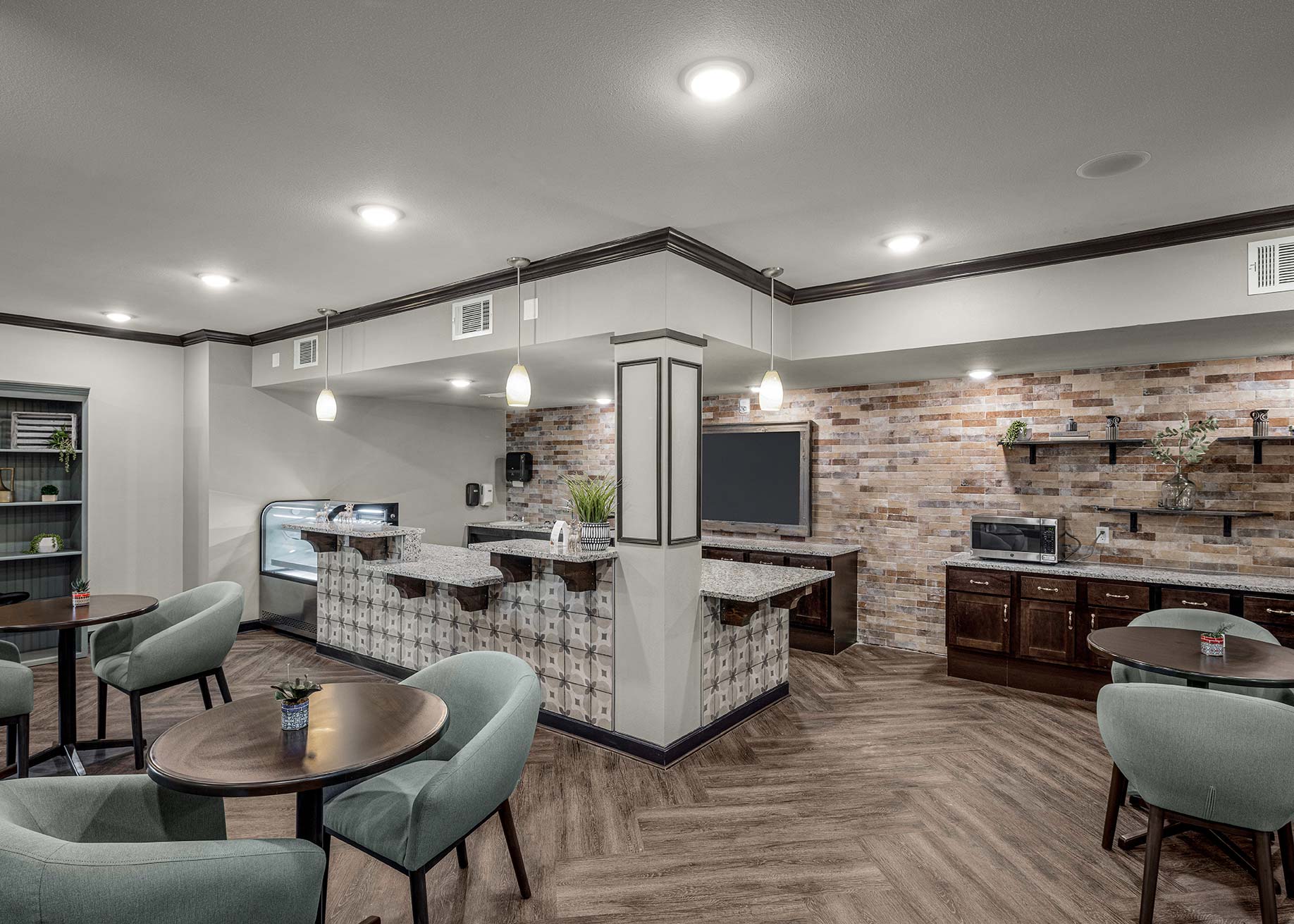 Senior living café and dining area with tile-front serving counter, wood cabinetry, pendant lighting, and comfortable seating for residents.