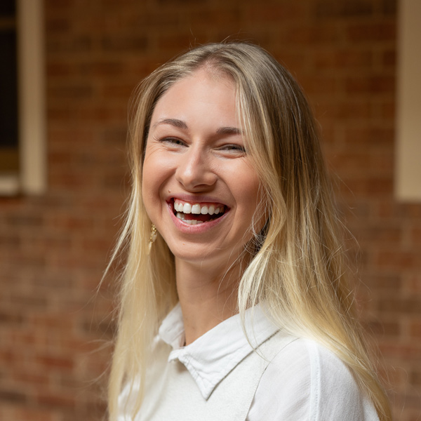 Kassie Pruitt, Resident Services Director at Pinnacle Groves Senior Living, smiling in a professional headshot, wearing a light blouse, with a softly blurred brick and window background.