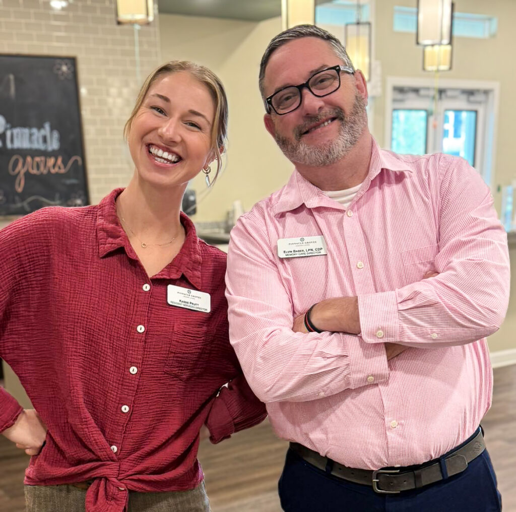 The Resident Services Director and Memory Care Director at Pinnacle Groves Senior Living smile brightly during a relaxed, proud moment.