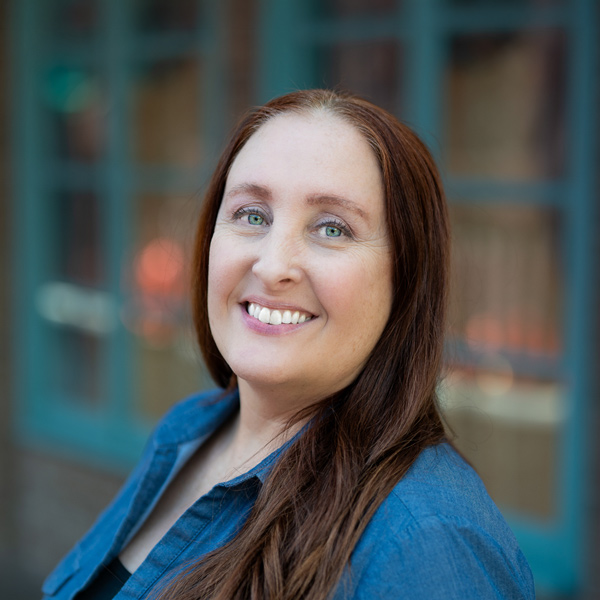 Toni Morgan, Wellness Director at Pinnacle Groves Senior Living, smiling in a professional headshot, wearing a blue top, with a softly blurred outdoor background featuring windows and brick details.